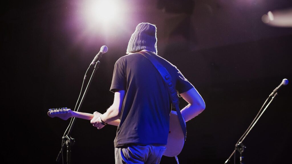 A young man plays guitar while a spotlight shines on him.