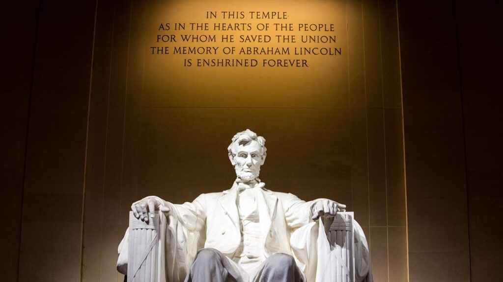 A view of the Lincoln Memorial, with the sculpture of Abraham Lincoln seated with the following words engraved on the wall behind him: "In this temple as in the hearts of the people for whom he saved the union the memory of Abraham Lincoln is enshrined forever."
