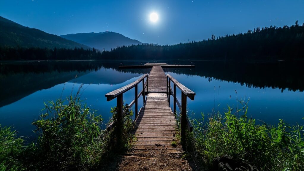 A deck leading out onto a lake, light up by the light of the moon.