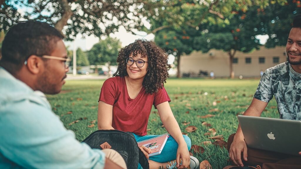 Three young people sit on the grass, engaged in friendly conversation.